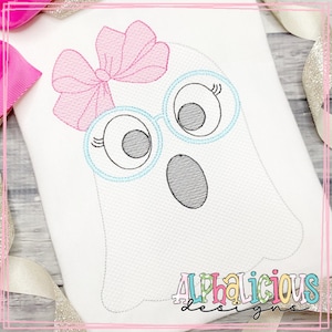 Pode incluir: Desenho bordado de um fantasma branco usando óculos azuis e um laço rosa. O fantasma tem olhos grandes e uma boca pequena. O desenho está sobre um fundo de tecido branco.