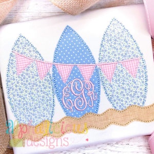 May include: Three blue and white patterned Easter eggs with pink and white gingham bunting. The middle egg has a pink monogram "GGJ" embroidered on it.