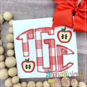 Peut inclure: Un t-shirt blanc avec un monogramme "TG" en damier rouge et blanc et deux motifs de pommes rouges. Le texte "alphalicicious designs" est visible dans le coin inférieur droit.