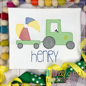 Pode incluir: Desenho bordado de um trator verde puxando uma bola de praia com o nome "henry" embaixo.