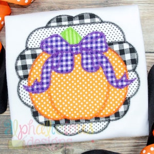 May include: A white shirt with a black and white checkered pumpkin applique. The pumpkin has a purple bow and orange polka dots.