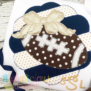 May include: A brown and white football with white stitching and a gold bow on top. The football is on a blue and gold striped background with white polka dots.