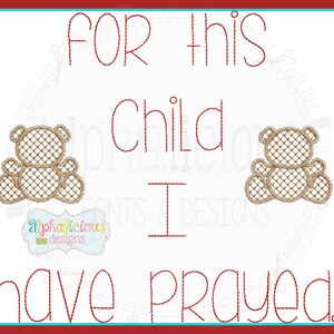 Op de afbeelding: Rood geborduurd ontwerp met de tekst "For this child I have prayed." Twee bruine teddyberen bevinden zich aan weerszijden van de tekst. Het ontwerp is op een witte achtergrond.