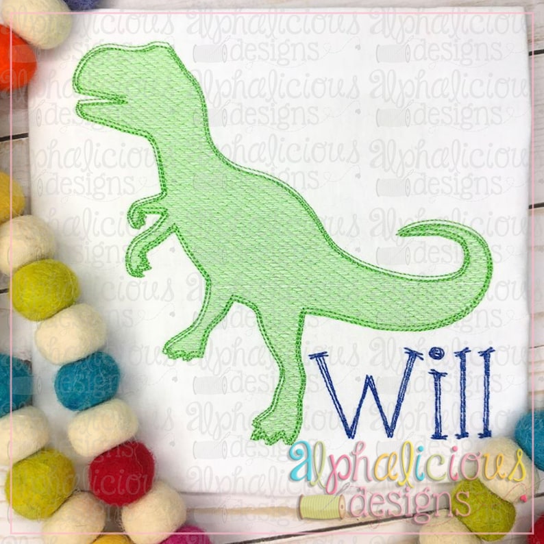 May include: Green dinosaur outline embroidery design with the name "Will" stitched in blue below. The design is on a white fabric background.