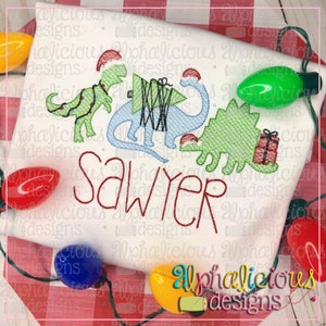 May include: Embroidered design of three dinosaurs wearing Santa hats, carrying a Christmas tree and presents. The name "Sawyer" is embroidered below the dinosaurs.