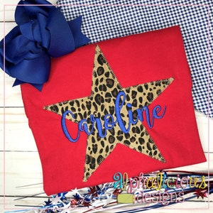May include: Red t-shirt with a large, five-pointed star made of leopard print fabric. The star has the name "Caroline" embroidered in blue cursive lettering.