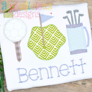 Puede incluir: Una camisa blanca con un campo de golf verde, una bola de golf en un tee y una bolsa de golf azul y blanca con palos de golf. El nombre "Bennett" está bordado en azul debajo de los artículos de golf.