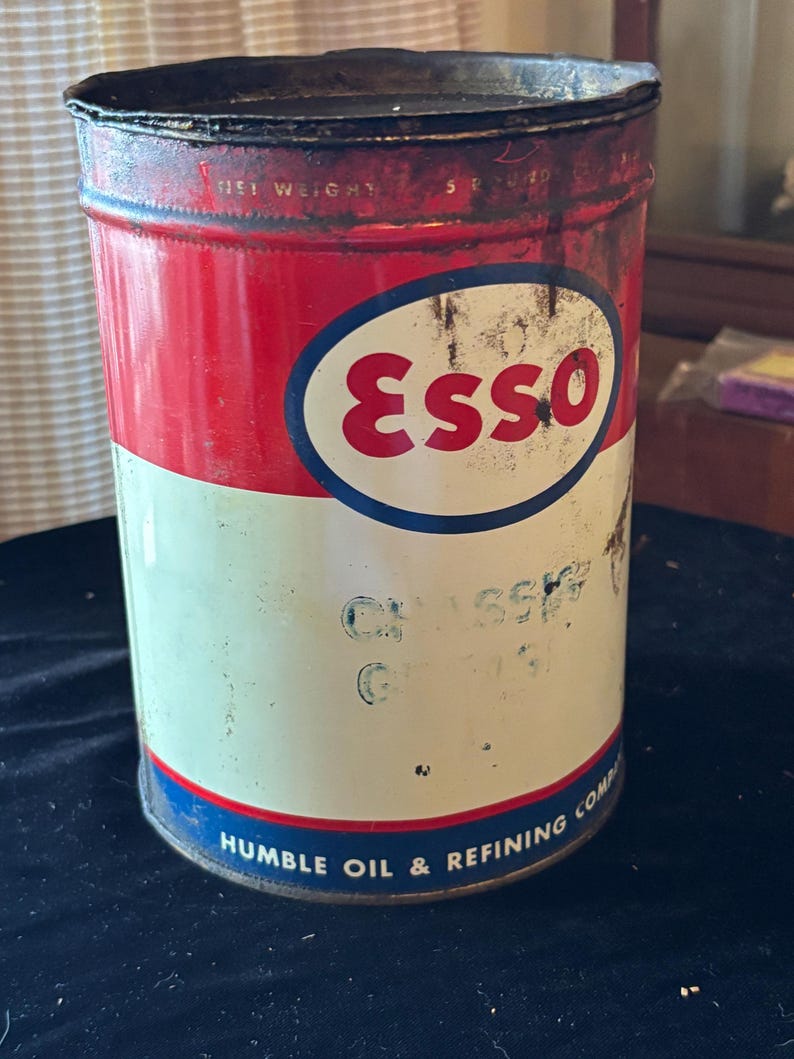 May include: Vintage Esso oil can with a red and white color scheme. The can features the Esso logo in a blue oval and text that reads "HUMBLE OIL & REFINING COMP". The can shows signs of wear and tear.