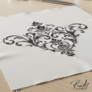 May include: A square, off-white fabric piece with a detailed, dark gray embroidered floral design. The embroidery features swirling vines, leaves, and floral elements. The bottom right corner has the text "Rivus Art EMBROIDERY".