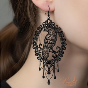 May include: Black raven earrings with a filigree design. The earrings showcase a raven within an oval frame, with dangling teardrop details. The intricate, lace-like design gives the earrings a gothic and elegant appearance.