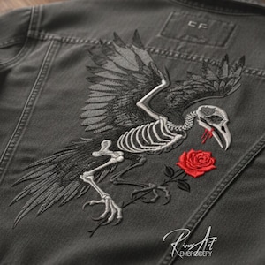 Pode incluir: Casaco de ganga cinzento escuro com um desenho bordado de um esqueleto de corvo segurando uma rosa vermelha. O corvo tem as asas abertas. O casaco tem as iniciais "CF" nas costas e a assinatura do bordador.