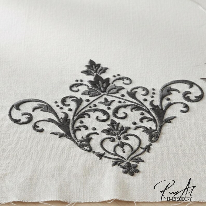 May include: Close-up of a detailed, dark gray embroidered floral design on a white fabric. The embroidery features a symmetrical pattern of leaves, swirls, and dots, with a heart-shaped element at the center. The design is likely for home decor or textile crafts.