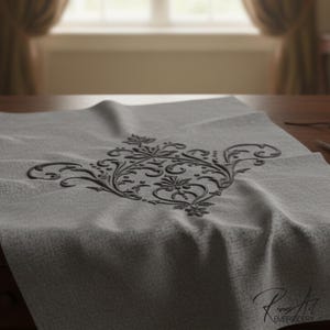 May include: A gray fabric with a black floral embroidery design is displayed on a wooden table. A pair of gold scissors and a pair of glasses are on the table. The fabric has a textured appearance.