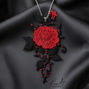 Könnte beinhalten: Halskette mit silberner Kette und Anhänger mit roter Rose und schwarzen Blättern. Die Rose ist der Mittelpunkt, mit aufwendigen Details. Der Hintergrund ist ein schwarzer, strukturierter Stoff.