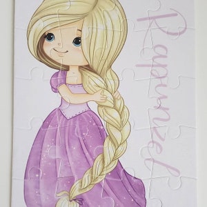 May include: A purple and white jigsaw puzzle featuring a cartoon girl with long blonde hair. The puzzle is titled "Rapunzel".