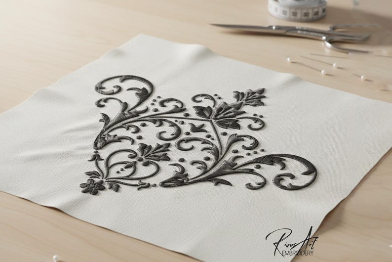 May include: A corner embroidery design in dark gray on a white fabric. The design features swirling floral and leaf patterns. Scissors, pins, and a measuring tape are in the background. The text "Rinus Art Embroidery" is in the lower right corner.
