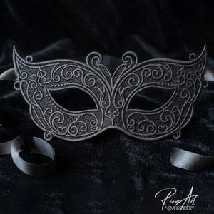 May include: A silver and black masquerade mask with intricate scrollwork and a matching black ribbon. The mask is set against a dark, textured background, creating a dramatic effect. The mask is a decorative item.