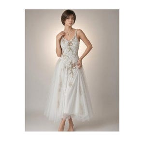 May include: A white midi-length dress featuring a sleeveless bodice with a V-neckline, adorned with intricate floral embroidery and lace detailing. The skirt is constructed from layers of sheer tulle, creating a voluminous silhouette.