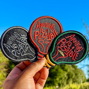 May include: Three embroidered iron-on patches in the shape of light bulbs with the text "Anything is Possible" in black, red, and green lettering.