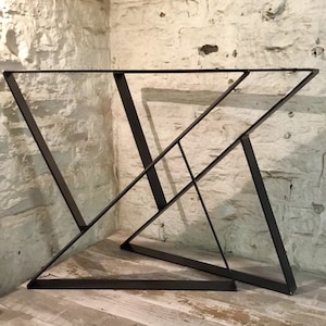 May include: Two black metal table legs with a geometric design. The legs are made of thick metal and have a matte black finish.