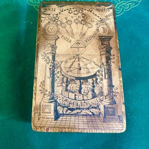 May include: A rectangular, antique-looking card with intricate illustrations and text. The card features two ornate columns, celestial symbols, and the words "SUPERIUS" and "PATER". The color palette is primarily sepia tones with dark blue accents.