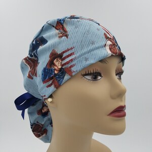 May include: A blue surgical scrub hat with a patriotic print featuring cowboys and stars. The hat has a blue ribbon tie.