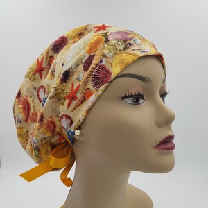 May include: A yellow, orange, and red patterned surgical scrub hat with a yellow tie. The pattern features seashells and starfish.