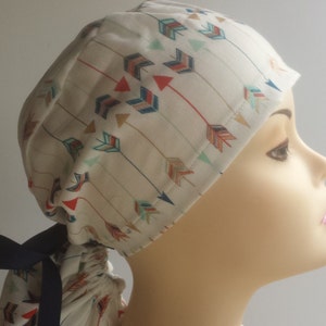 May include: A white surgical scrub hat with a colorful arrow pattern. The hat has a navy blue tie.