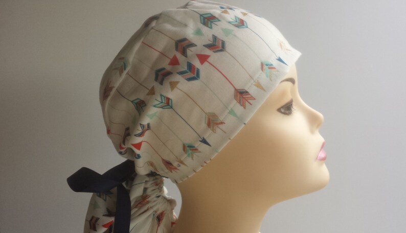 May include: A white surgical scrub hat with a colorful arrow pattern. The hat has a navy blue tie.