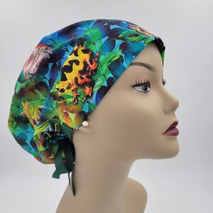 May include: A blue, green, and yellow surgical scrub hat with a frog print. The hat has green ties.