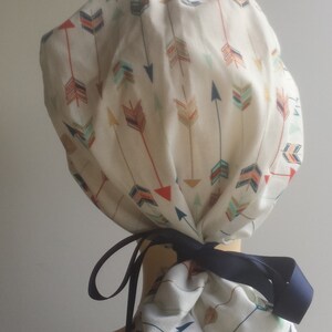 May include: A white scrub cap with a colorful arrow print. The cap has a navy blue ribbon tie.