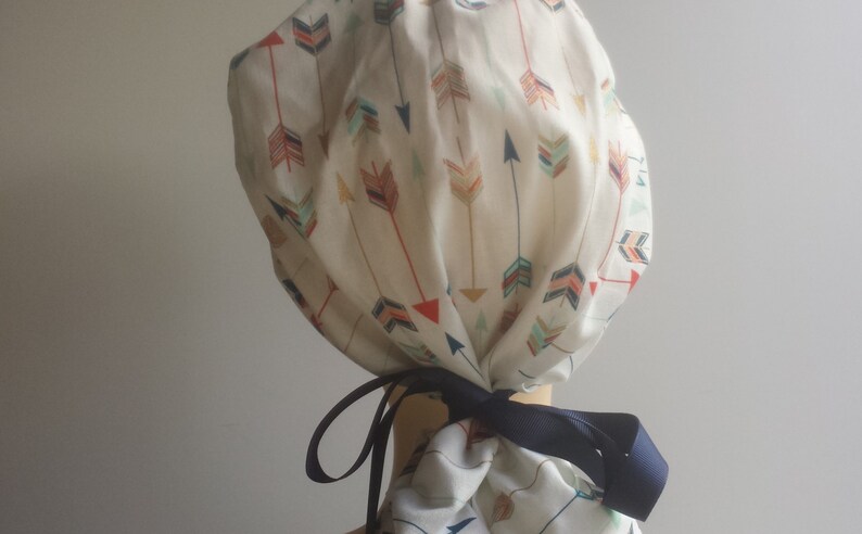 May include: A white scrub cap with a colorful arrow print. The cap has a navy blue ribbon tie.
