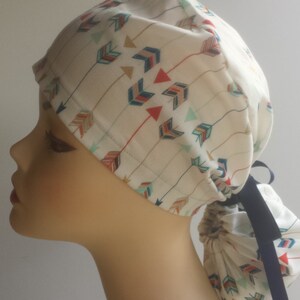 May include: A white scrub hat with a colorful arrow pattern and a black tie. The hat is tied at the back of the head.