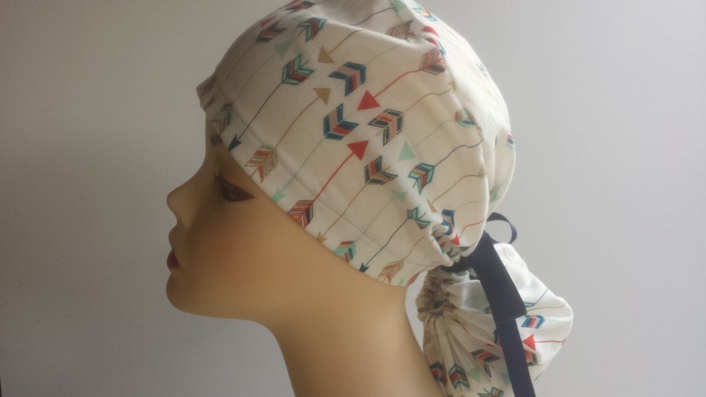 May include: A white scrub hat with a colorful arrow pattern and a black tie. The hat is tied at the back of the head.