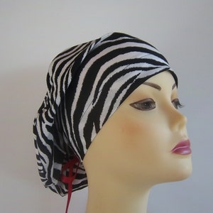 May include: A black and white zebra print surgical scrub hat with a red tie. The hat is made of a soft, comfortable fabric and is designed to be worn by medical professionals.