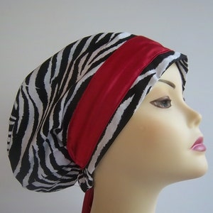 May include: A black and white zebra print satin sleep cap with a red satin ribbon. The cap is tied at the back with a long ribbon.