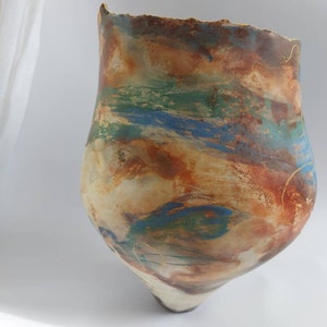 Könnte beinhalten: Eine Keramikvase mit einem abstrakten Design in Braun-, Blau-, Grün- und Goldtönen. Die Vase hat eine einzigartige, unregelmäßige Form und eine strukturierte Oberfläche.