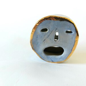 May include: A ceramic face sculpture with a blue glaze and a gold rim. The face has a wide open mouth and closed eyes.