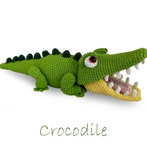 Pode incluir: Brinquedo de crocodilo de crochê verde com a boca aberta amarela e a língua rosa. O brinquedo tem olhos pretos e um dorso com padrão verde e preto.