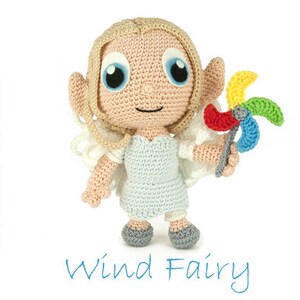 Op de afbeelding: Een gehaakte feepop met blond haar, die een lichtblauwe jurk draagt en een kleurrijk windmolentje vasthoudt. De pop staat op een witte achtergrond. De tekst "Wind Fairy" staat onder de pop.