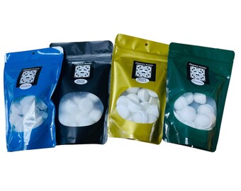 May include: Four bags of white wax melts in different scents. The bags are blue, black, gold, and green. The bags have a clear window to see the wax melts inside. The bags have labels with the text "Pleasure Scents" and the scent name.