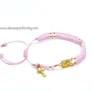 May include: A pink beaded bracelet with a gold-colored cross charm and a gold-colored rectangular charm. The bracelet is adjustable with a pink cord. The text "www.alexassparkle.etsy.com" is visible.