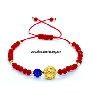 May include: Red string bracelet with a gold St. Michael medal and a blue evil eye charm. The bracelet is adjustable and has a knot closure.
