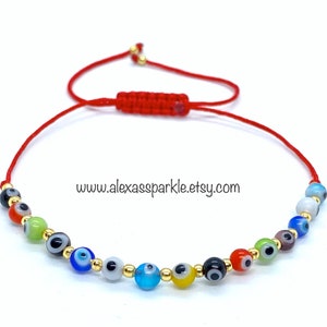 May include: Red string bracelet with a variety of colorful evil eye beads. The beads are made of glass and have gold accents. The bracelet is tied with a knot and has a tassel.
