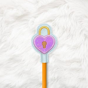 May include: A pencil topper shaped like a heart-shaped lock. The lock is purple with a gold keyhole and a gold arched handle. The lock is outlined in light blue with gold stitching. The pencil is orange.