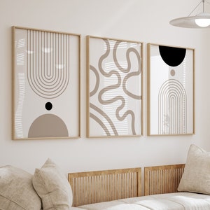 May include: Three framed abstract art prints with beige and brown geometric designs. The prints are displayed above a light-colored sofa with matching pillows. The room has a neutral color palette with a modern aesthetic.