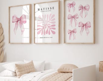 Könnte beinhalten: Drei gerahmte Kunstdrucke mit Aquarelldesigns. Ein Druck zeigt eine rosa Schleife, ein anderer den Text "MATISSE PAPIERS DECOUPES" und ein rosa abstraktes Design, und der dritte zeigt mehrere rosa Schleifen. Die Rahmen sind aus hellem Holz.