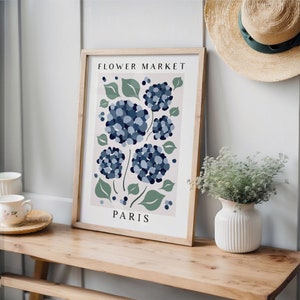 May include: A framed print with a floral design featuring blue hydrangeas and green leaves. The print has the text "FLOWER MARKET PARIS" on it.