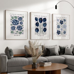 May include: Three framed prints with a pink background and blue floral illustrations. The prints are titled "Flower Market" with the cities "Paris", "Tokyo", and "New York" listed below the flowers.