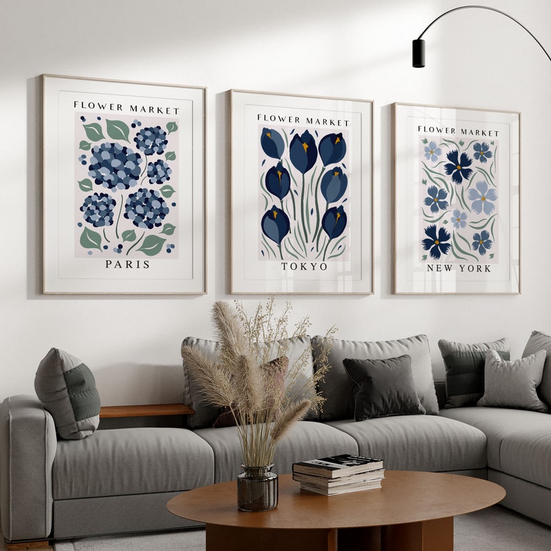 May include: Three framed prints with a pink background and blue floral illustrations. The prints are titled "Flower Market" with the cities "Paris", "Tokyo", and "New York" listed below the flowers.